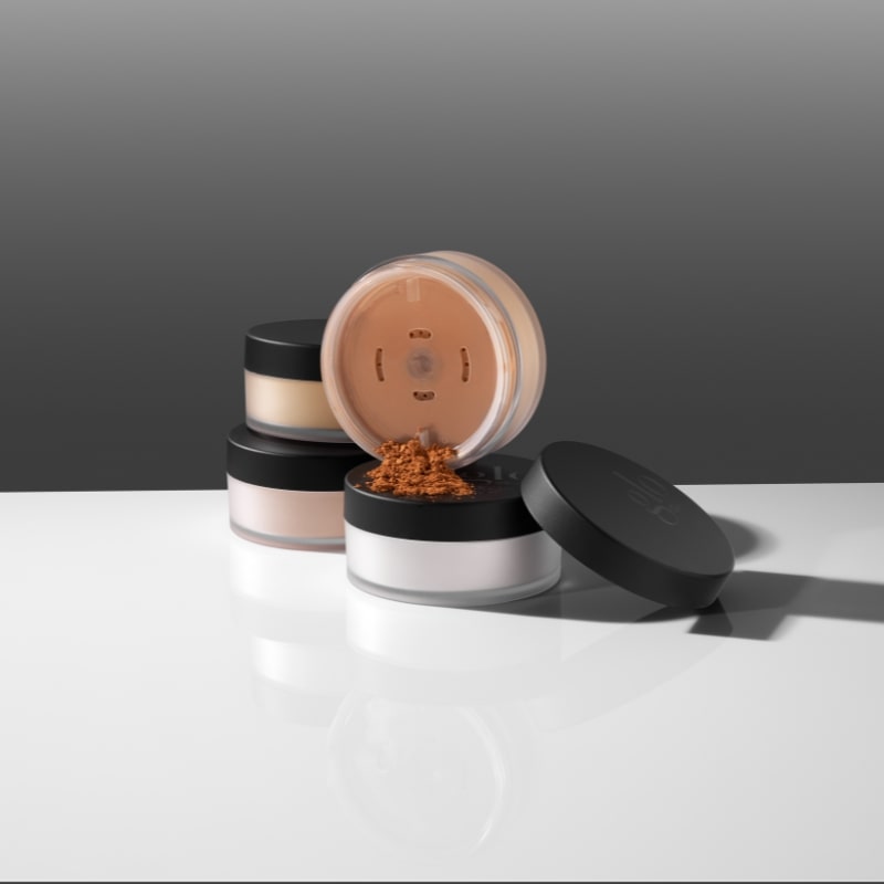Three translucent jars of cosmetic loose powder with black lids, one open and spilled terracotta powder on white surface