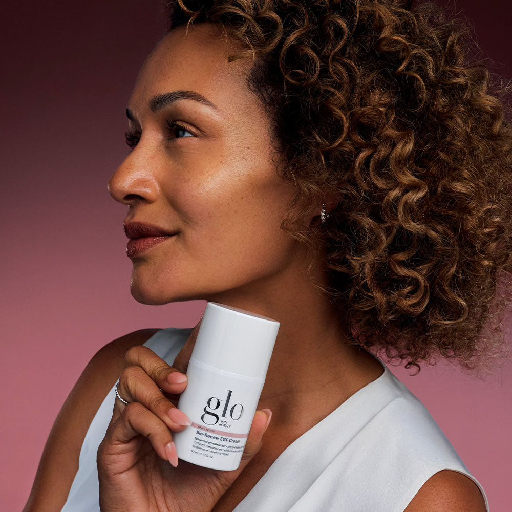 Close-up of Bio-Renew EGF Cream pump bottle held by a model showing the white glo packaging against a mauve gradient background