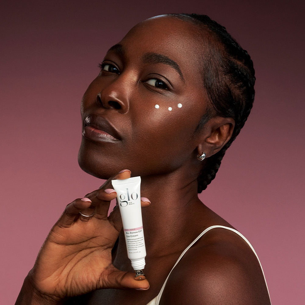Angled view of Bio-Renew EGF Eye Cream tube showing stainless steel applicator tip and three dots of cream under model’s eye with mauve background