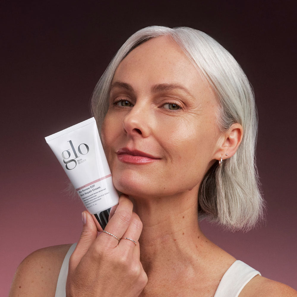 Angled front view of Bio-Renew EGF Rich Repair Cream tube showcasing Glo logo and silver cap held by a model against a gradient mauve background