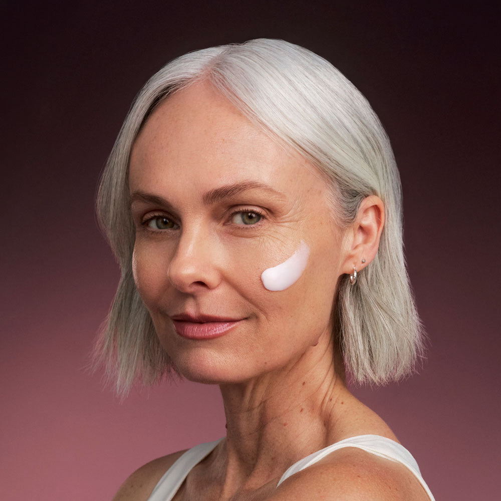 Woman with silver hair showing a dab of Bio-Renew EGF Rich Repair Cream on her cheek against a mauve gradient background