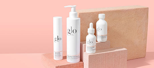 Skincare bottles labeled 'glo' arranged on a pink backdrop with stacked textured blocks.