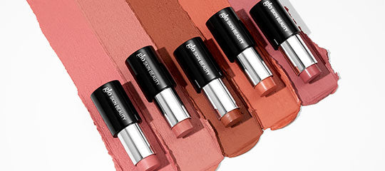 Six nude-to-rose lipsticks on smeared matching swatches; black caps labeled bareMinerals