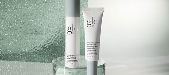Two glo skincare tubes displayed on a glass pedestal with textured green background