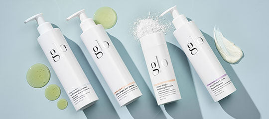 Four white bottles labeled 'glo' with cleanser, powder and cream swatches on a blue background