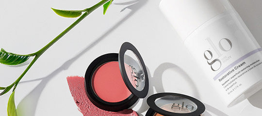 Two open glo compacts with pink cream, a glo Restorative Cream bottle, green leaves and a swatched blush.