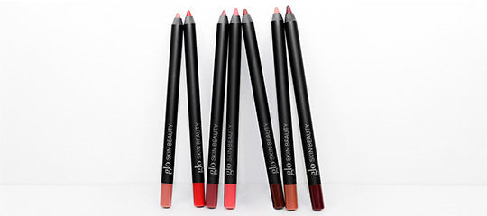 Six black lip liners in nude, pink, red and burgundy shades arranged upright on a white background