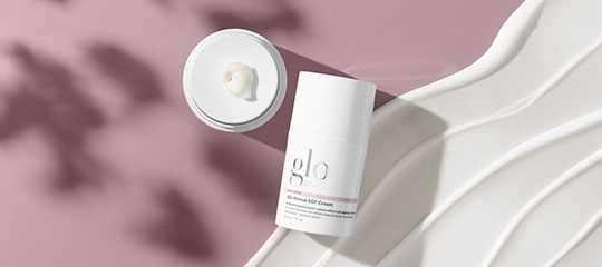 glo skincare stick and open cream jar on pink background beside white sculpted tray