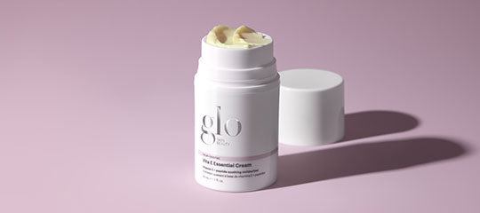 White cosmetic cream stick labeled glo, cap beside it, cream exposed on pale pink background.