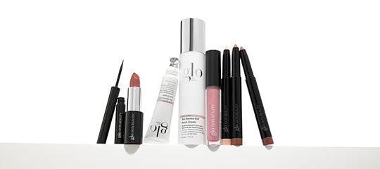 Assorted glo cosmetics: eyeliner, lipstick, lip liners, lip gloss, and skincare bottles on a white surface