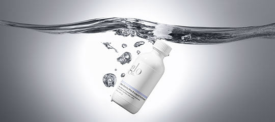 White bottle labeled glo partially submerged under water with rising bubbles