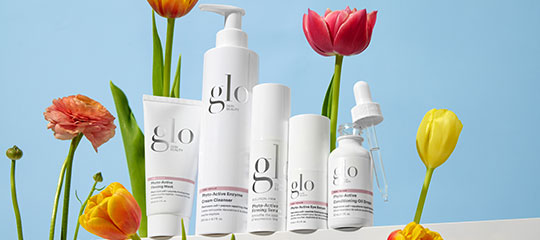 glo skincare product lineup — bottles and tubes arranged with tulips on a blue background.