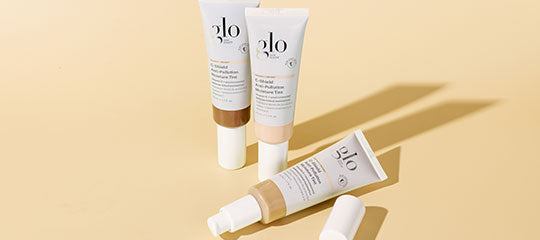 Three Glo Skin Beauty C-Shield Moisture Tint tubes showing shade variations and a pump on pale yellow background