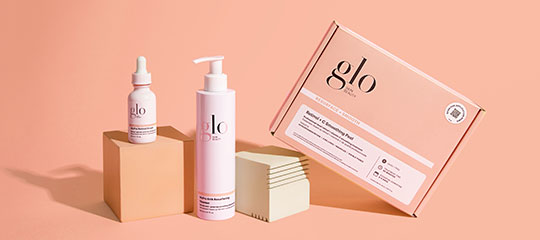 glo skincare set: peach box, pump bottle, and dropper bottle arranged on pedestal blocks