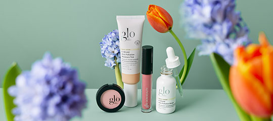 glo skincare products (compact, tube, lip gloss, dropper bottle) styled with tulips and hyacinths