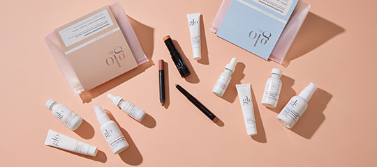 Assorted glo skincare and makeup products laid out on peach background, bottles, tubes, pencils and boxed sets
