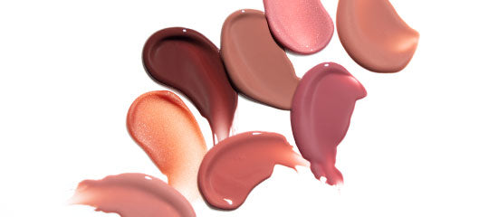 Creamy lipstick and lip gloss swatches in pink and nude tones on a white background.