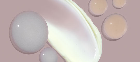 Cream smear with translucent serum droplets on mauve background.