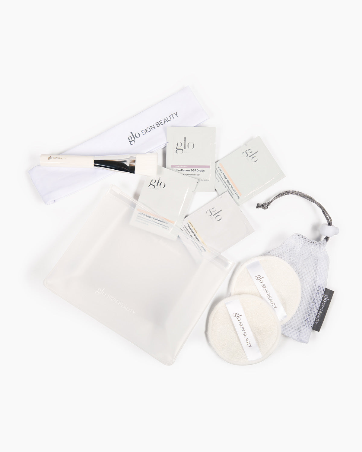 Top-down view of Spa Day Sampler Kit with frosted zip pouch, sample sachets, brush, headband and reusable cleansing pads