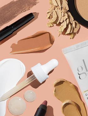 Makeup layout on peach background: dropper, foundation and concealer swatches, compact powder, and a white tube labeled 'gl'.