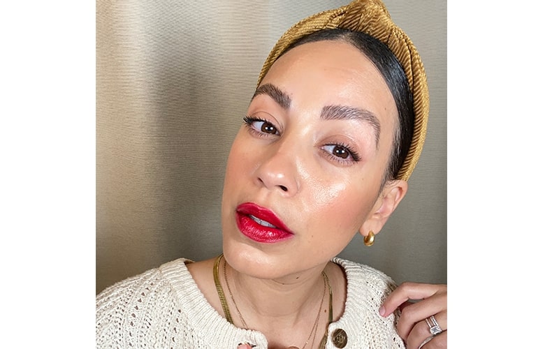 Woman wearing glossy classic red lipstick with gold headband and earrings, cream knit sweater