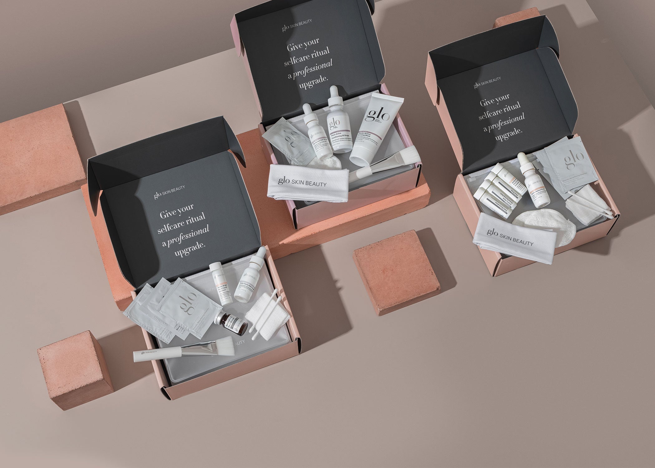 Three open pink boxes of glo SKIN BEAUTY kits with products; lids read 'Give your selfcare ritual a professional upgrade.'