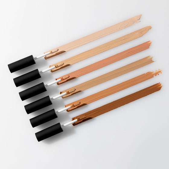 Six concealer wands with diagonal swatches showing light-to-deep skin shades and matte black caps