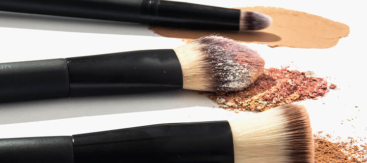 Three makeup brushes, loose bronze and beige powder, and two foundation swatches on white background.
