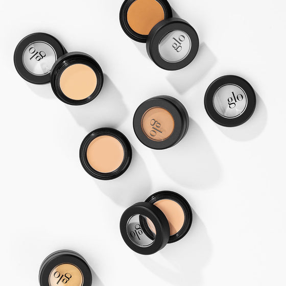 Scattered black compacts of glo camouflage cream in assorted skin shades, lids showing glo logo.