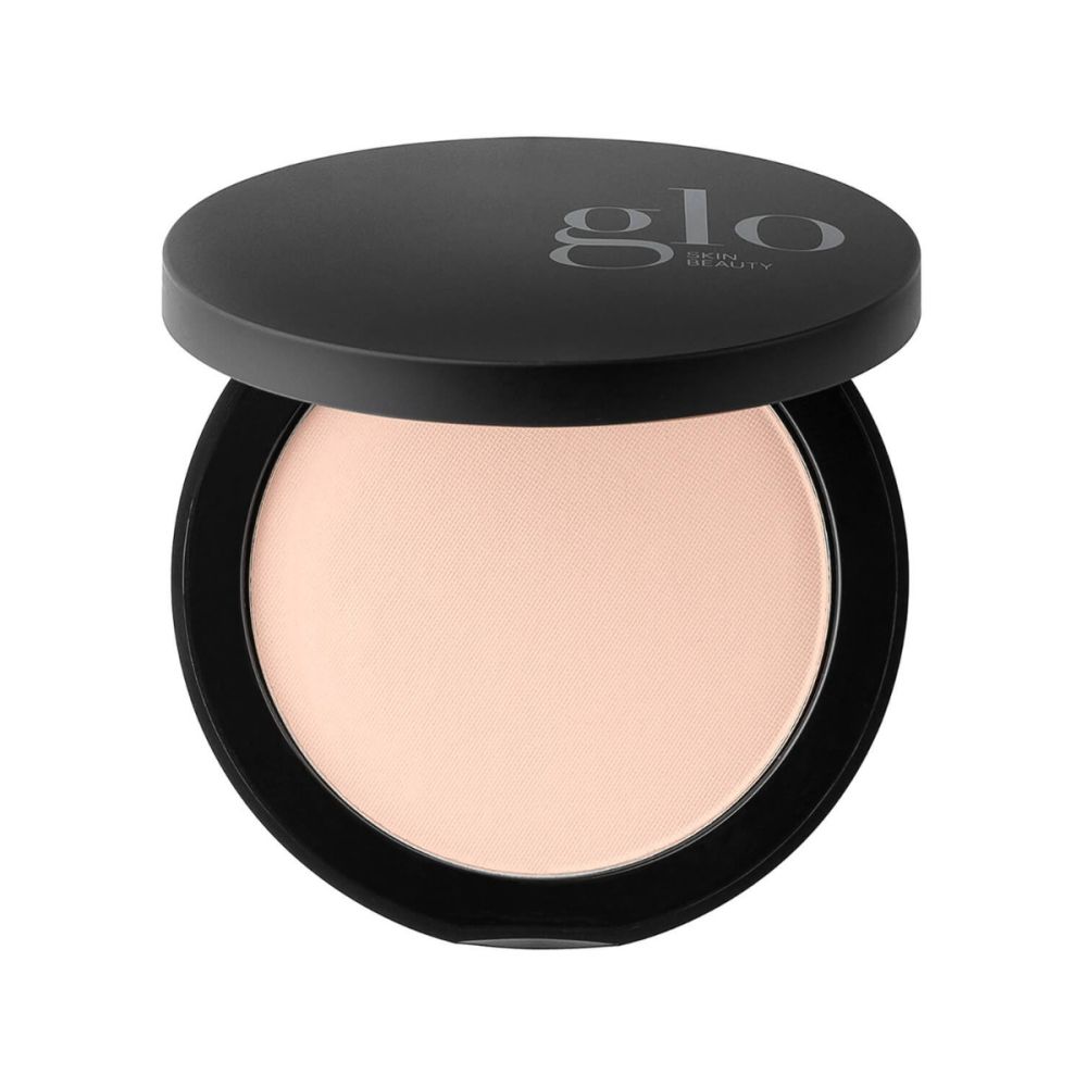 Angled top view of Pressed Base compact showcasing light beige pressed powder in a black case on white background