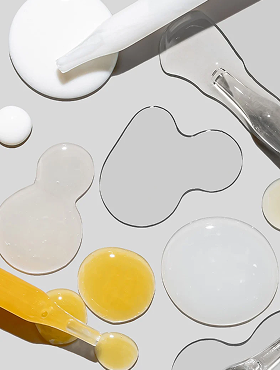 Clear and golden cosmetic serum droplets with glass pipettes and a white spatula on a light gray background