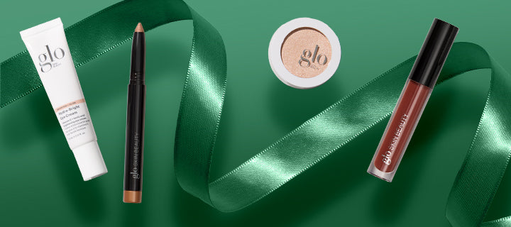 Makeup products labeled 'glo'—tube, pencil, pressed powder and lip gloss—arranged on green background with satin green ribbon