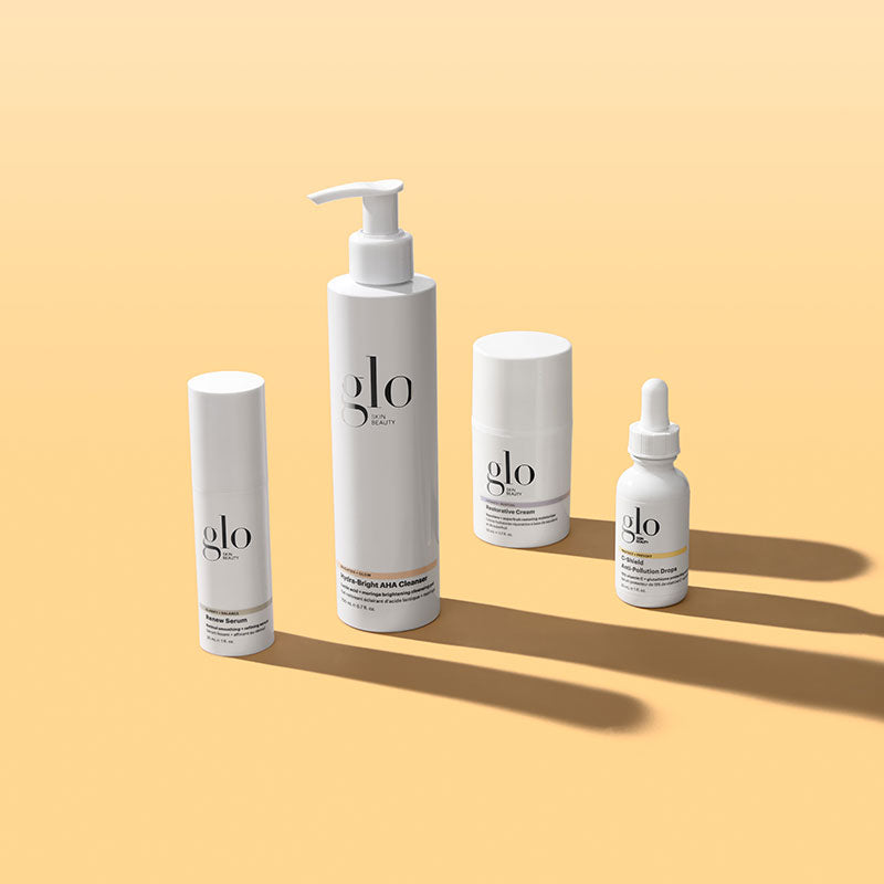 Front view of four Glo Skin Beauty skincare products showcasing white packaging and long shadows on peach background