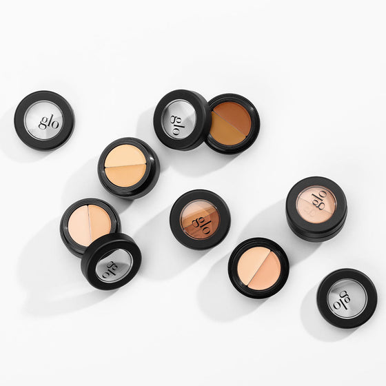 Several round two-shade concealer compacts with glo logos on lids, scattered on a white background