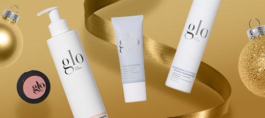 Skincare and makeup bottles and compact labeled glo and glo skin on gold background with ribbon and holiday ornaments.
