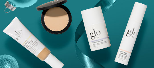 glo makeup and skincare: foundation tube, compact powder, two bottles on teal background with ribbon and ornaments.